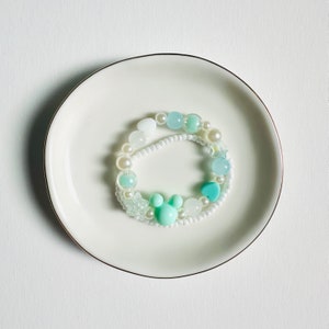 May include: A white and light blue beaded bracelet with a light blue heart charm and a light blue Mickey Mouse charm.