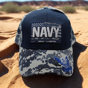 Könnte beinhalten: Eine marineblaue Baseballkappe mit einem rechteckigen Aufnäher, der das Wort NAVY in weißen Großbuchstaben auf einem digitalen Tarnmuster zeigt. Der Schirm und die Seitenteile haben einen grau-schwarzen Digitaltarnaufdruck mit einem blauen Adler.