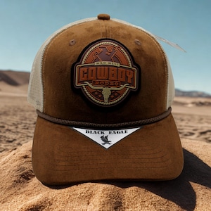 Peut inclure: Casquette de camionneur marron et beige avec un écusson "Cowboy Rodeo". L'écusson représente un crâne de taureau et les mots "Wild West Cowboy Rodeo". La casquette a une visière incurvée et un dos en filet. Une étiquette avec "Black Eagle" est attachée.