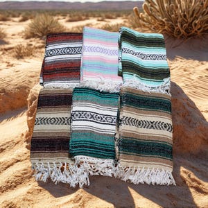 May include: A collection of six folded woven blankets featuring various striped patterns in colors including red, white, black, pink, light blue, teal, and brown. Each blanket has a textured fabric finish and white fringe along the bottom edge.