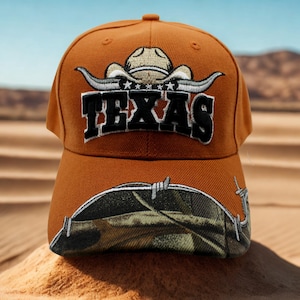 May include: An orange baseball cap featuring an embroidered white cowboy hat above the black text TEXAS. The brim displays a camouflage pattern overlaid with a graphic of barbed wire. The cap has a structured crown and a curved visor design.