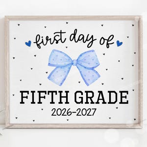May include: A rectangular sign in a light wood frame featuring the text "first day of" in black script, a large light blue polka-dot bow, and the text "FIFTH GRADE" and "2026-2027" in black block letters, all on a white background with small black hearts.