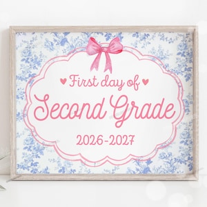 Puede incluir: Un letrero rectangular en un marco de madera clara con un fondo floral azul y blanco. Un borde festoneado rosa rodea el texto "First day of Second Grade" y "2026-2027" en letra cursiva rosa, coronado con un lazo de acuarela rosa y dos corazones.