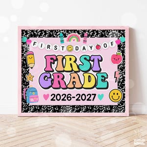 May include: A rectangular sign with a pink background and black and white composition notebook border. It features the text FIRST DAY OF FIRST GRADE 2026-2027, decorated with colorful illustrations of a rainbow, pencil, apple, and backpack.