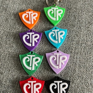 Op de afbeelding: Acht sleutelhangers met een schildvorm en de letters "CTR" in wit op een gekleurde achtergrond. De sleutelhangers zijn in de kleuren oranje, groen, paars, blauw, groen, paars, rood en zwart.