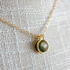 Op de afbeelding: Een gouden ketting met een ronde, donkergroene hanger met gouden accenten. De hanger heeft een glinsterend, iriserend effect.