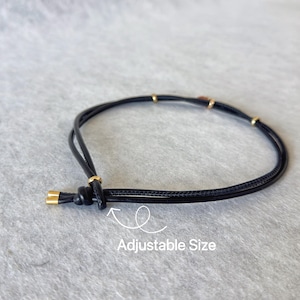 May include: Black adjustable bracelet with gold-coloured accents. The bracelet has a knotted design and small gold beads. The text "Adjustable Size" is visible in the image.
