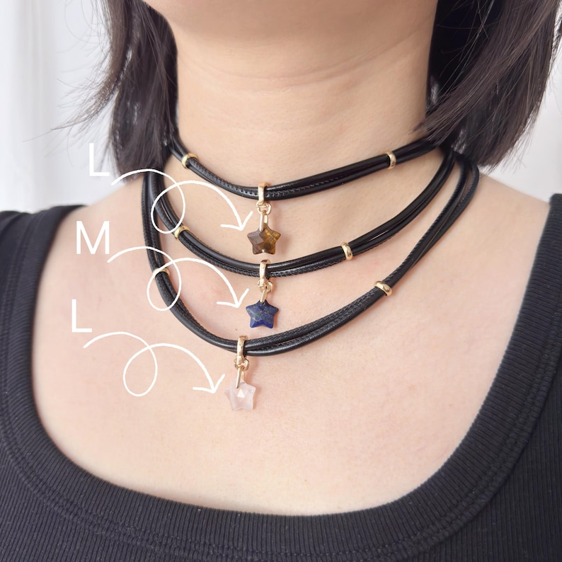 May include: Three black choker necklaces with star-shaped pendants in brown, blue, and pink. Each necklace features gold-coloured accents and a clasp. The necklaces are layered and worn around the neck.