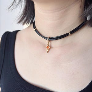 May include: Black choker necklace with a gold pendant. The pendant is a star shape with an orange center. The necklace has gold accents and is worn around the neck.