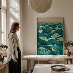Pu&ograve; includere: Stampa artistica incorniciata raffigurante onde oceaniche stilizzate nei toni del verde acqua e bianco. L'opera d'arte ha un'estetica vintage, con accenti dorati e una cornice marrone chiaro. La stampa &egrave; su un tavolo bianco.
