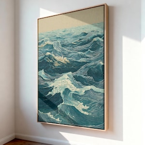 May include: A framed artwork depicting a stylized ocean scene. The artwork features detailed linework in shades of blue and white, creating a textured appearance of waves. The frame is a light wood color, adding a natural touch to the piece.