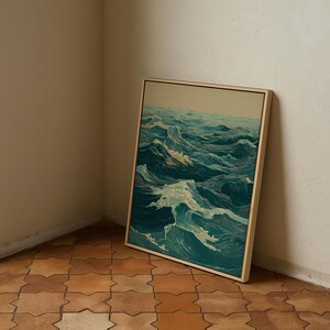 May include: A framed artwork depicting a dynamic ocean scene with rolling waves in shades of teal and white. The artwork is displayed in a light-colored wooden frame, leaning against a neutral-toned wall. The floor is tiled with a geometric pattern.