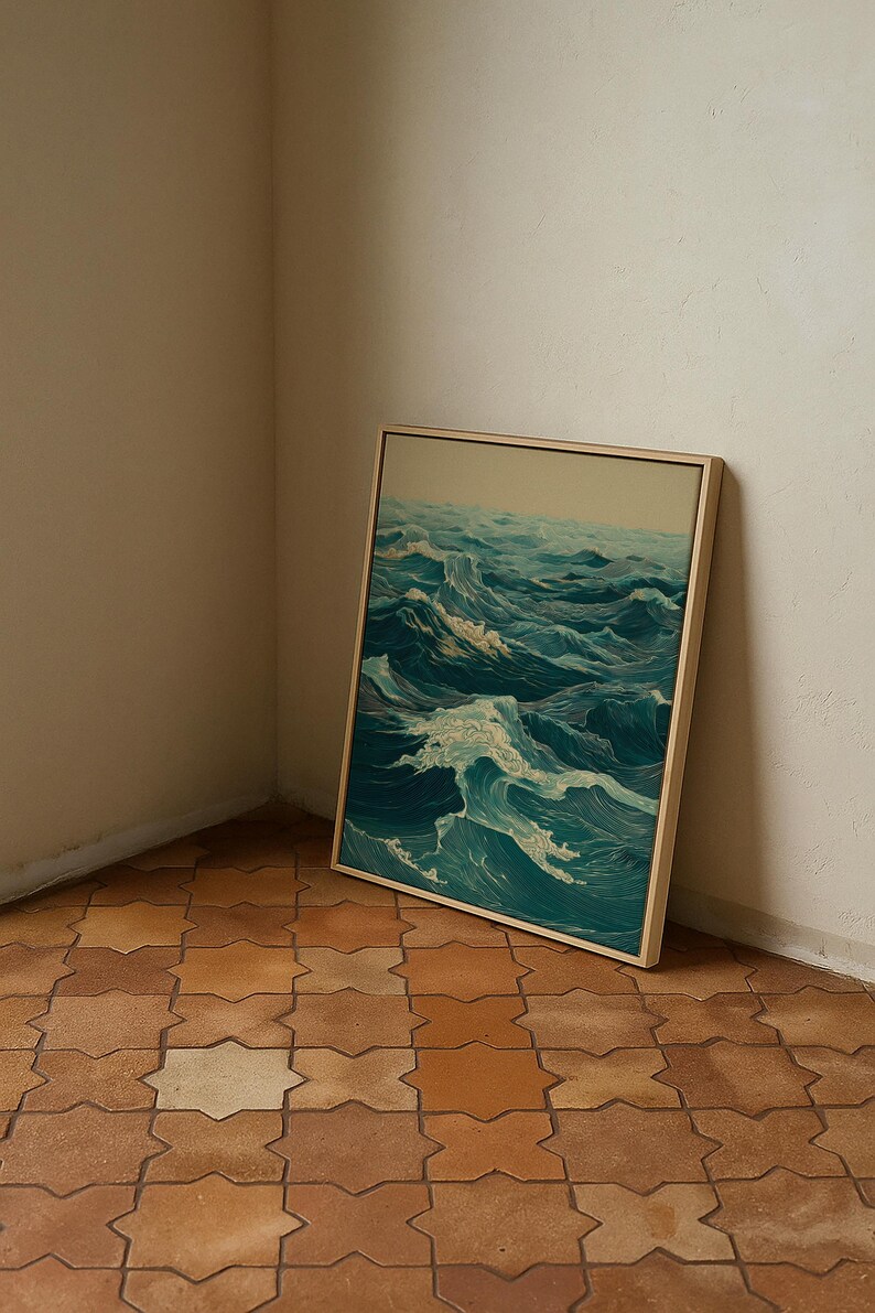 May include: A framed artwork depicting a dynamic ocean scene with rolling waves in shades of teal and white. The artwork is displayed in a light-colored wooden frame, leaning against a neutral-toned wall. The floor is tiled with a geometric pattern.
