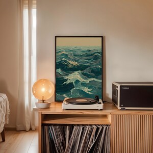 May include: A framed art print depicting ocean waves in shades of teal and white. A white record player with a black record sits on a wooden cabinet. A glowing orange globe lamp and a black audio component are also on the cabinet.