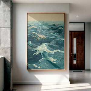 May include: A framed artwork depicting a detailed ocean scene with stylized waves in shades of blue and white. The artwork is in a gold-colored frame and hangs on a white wall. The overall theme is nautical and serene.