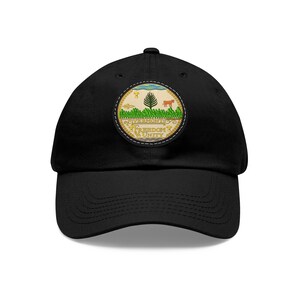 May include: A black baseball cap with a circular patch featuring the state seal of Vermont. The patch is yellow, green, and brown with the words "Vermont", "Freedom & Unity" and a pine tree and cow.