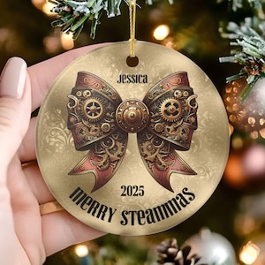May include: A round Christmas ornament with a steampunk bow design. The bow is detailed with gears and red accents. The ornament has the name "Jessica" and the year "2025" printed on it, along with the words "Merry Steammas".
