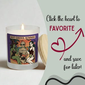May include: A lit candle in a glass jar with a wooden lid. The label reads "Hot Ghoul Summer" with illustrations of ghouls on a beach. The text "Click the heart to FAVORITE and save for later!" is also visible.