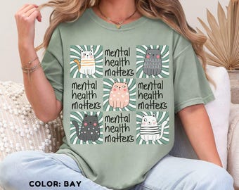 May include: A green t-shirt with a graphic of six cats and the text "mental health matters" repeated four times. The cats are all different colors and have different expressions.