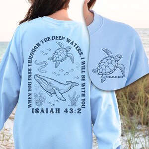 May include: Light blue sweatshirt with a marine-themed graphic. The design includes a whale, two turtles, fish, and the text "WHEN YOU PASS THROUGH THE DEEP WATERS, I WILL BE WITH YOU. ISAIAH 43:2".