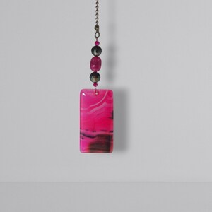 Op de afbeelding: Roze en zwarte agaat hanger met zilveren ketting en roze kralen. De hanger is rechthoekig en heeft een draaiende patroon.