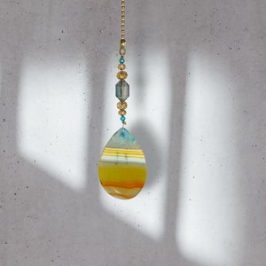 May include: A gold chain with a teardrop-shaped agate pendant. The agate is yellow, orange, and white with a blue stripe.