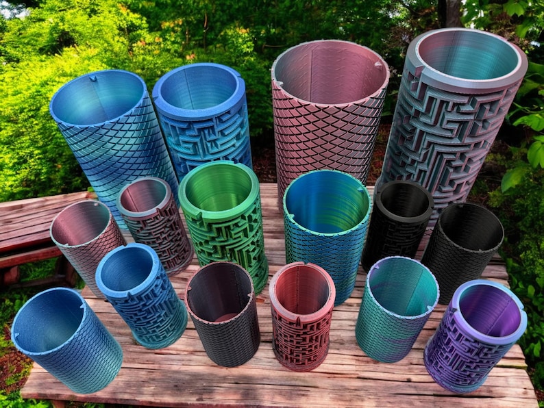 May include: A collection of 14 colorful cylindrical containers with various patterns, including a maze design, a scale pattern, and a geometric design. The containers are made of a smooth, hard material and are arranged on a wooden surface.