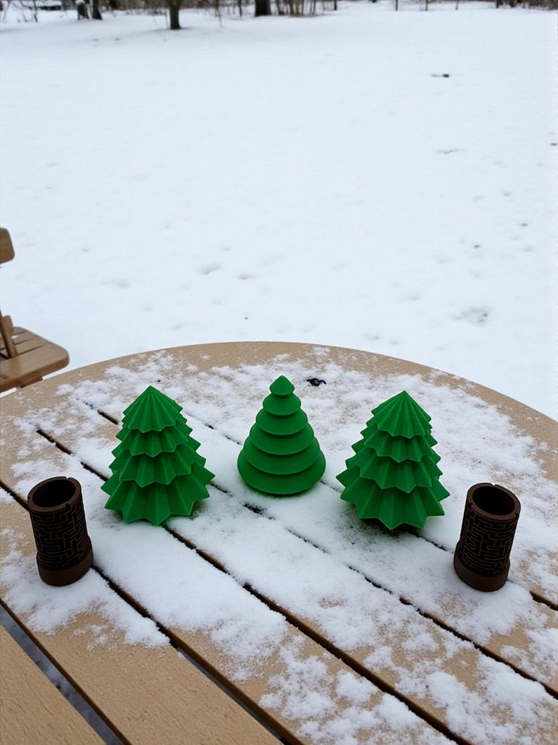 May include: Three green, stylized Christmas tree decorations and two brown cylindrical holders sit on a snow-covered wooden table. The trees have a layered design. The holders have a geometric pattern.