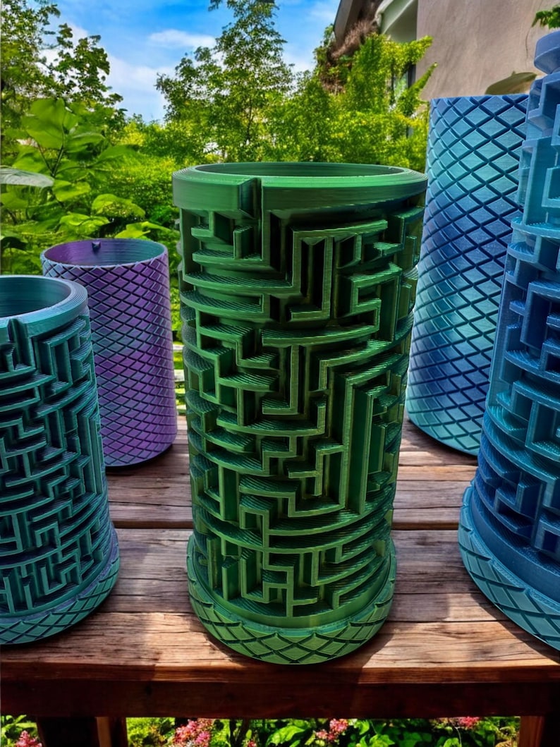 May include: A collection of cylindrical planters featuring intricate, raised maze patterns on the exterior. The planters are finished in various gradient colors, including metallic green, purple, and blue, with a diamond-textured base design.