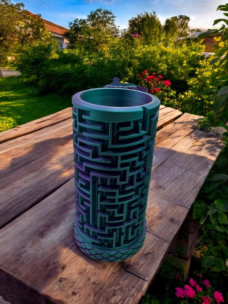 May include: A cylindrical container featuring a complex, three-dimensional maze pattern on its exterior surface. The object displays a gradient color shift from deep purple to teal, with a textured, diamond-patterned base and a smooth, circular rim.