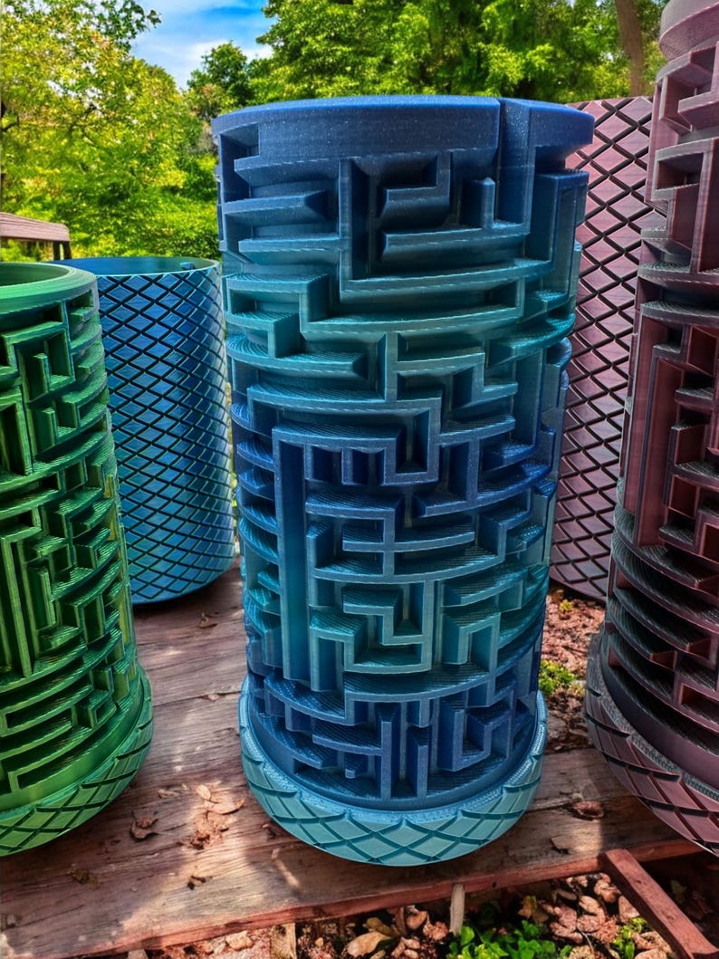 May include: A cylindrical 3D printed object featuring a complex, raised maze pattern on its exterior surface. The object displays a gradient of blue colors, transitioning from a lighter shade at the base to a deeper blue at the top, with a diamond-textured rim.