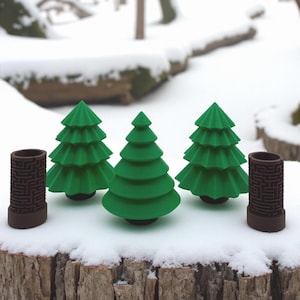 May include: Three green Christmas tree figurines and two brown cylindrical maze-patterned objects are arranged on a snowy surface. The trees have a classic conical shape, while the cylinders have a detailed design.