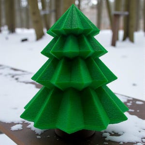 May include: A vibrant green, geometric Christmas tree decoration. The tree has a layered design with textured surfaces, set against a snowy outdoor backdrop. The tree is approximately 6 inches tall.