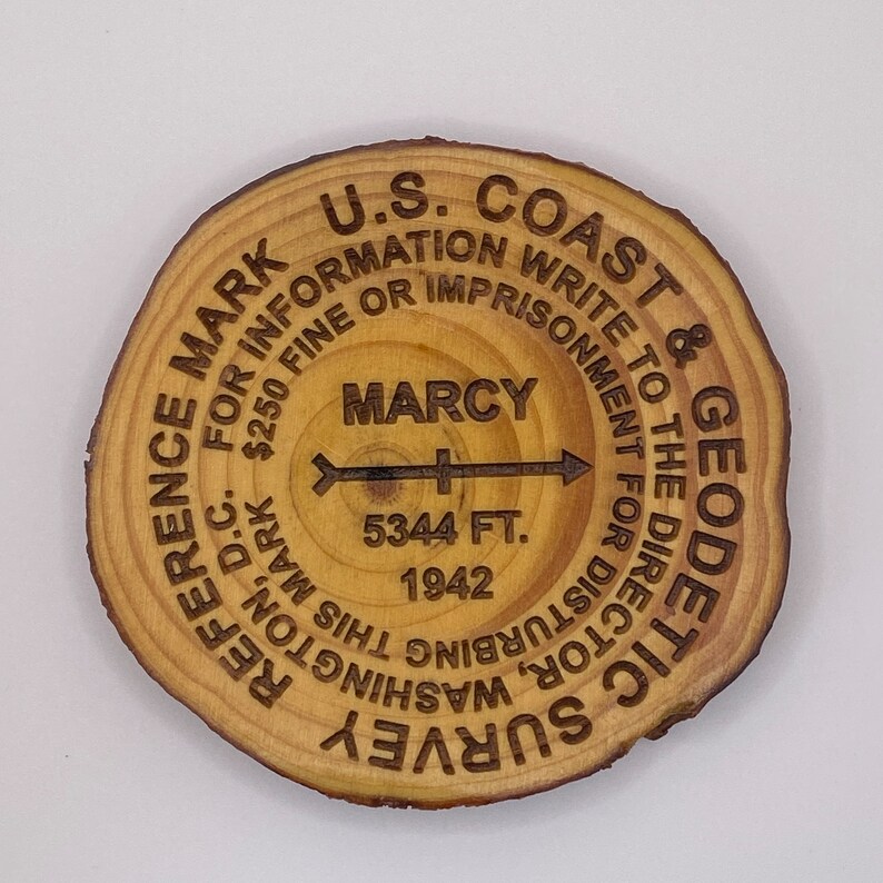 Puede incluir: Un disco de madera con el texto "U.S. Coast & Geodetic Survey" y "Reference Mark" alrededor del borde. El centro del disco tiene el texto "Marcy" y "5344 ft. 1942".