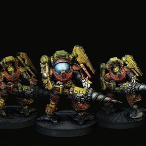 Könnte beinhalten: Drei Miniaturfiguren von Mechs in Kampfstellung. Die Mechs sind in Gelb, Rot und Braun bemalt und weisen detaillierte mechanische Merkmale auf. Jeder Mech ist auf einer kreisförmigen Basis montiert.