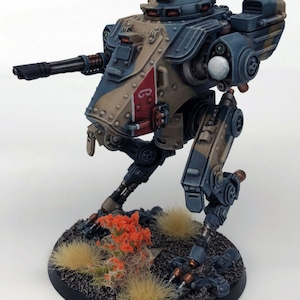 Könnte beinhalten: Eine detaillierte, handbemalte Miniatur eines laufenden Roboters oder Mechs mit einer großen Waffe. Der Roboter ist in einem Tarnmuster aus Tan, Blau und Rot bemalt. Der Roboter steht auf einer Basis mit braunem und grünem Gras.