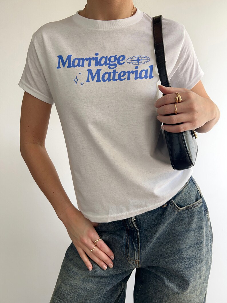 Puede incluir: Camiseta blanca con texto azul que dice "Marriage Material" y un gr&aacute;fico de globo terr&aacute;queo azul.