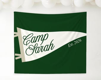May include: A dark green banner with a white pennant shape in the center. The pennant has the words "Camp Sarah" in a cursive font and "Est. 2026" in a smaller font. Beige accents are on the left side.