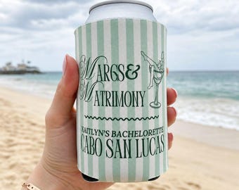 May include: A light green and white vertical striped foam can cooler featuring dark green text that reads Margs & Matrimony, Kaitlyn's Bachelorette, and Cabo San Lucas, along with a graphic of a person sitting inside a martini glass.