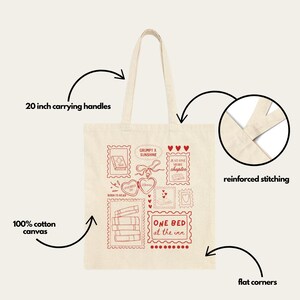 May include: Cream-colored tote bag with red stamp-like illustrations and text. Features include 20-inch carrying handles, reinforced stitching, and flat corners. The bag is made of 100% cotton canvas and has the text "GRUMPY X SUNSHINE" and "ONE BED at the inn".