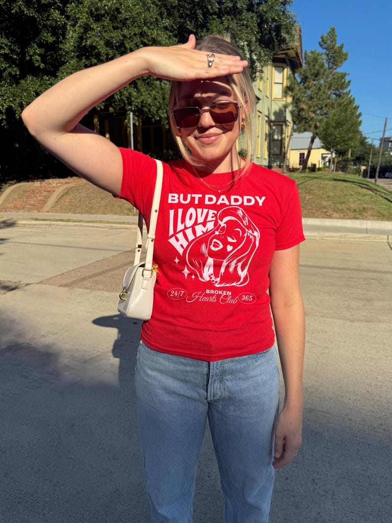 Puede incluir: Una camiseta roja con un estampado gr&aacute;fico blanco que dice "But Daddy I Love Him" y "24/7 Broken Hearts Club 365".