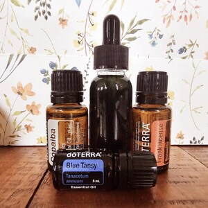 May include: Four small glass bottles of essential oils with black caps and droppers. The bottles are labeled "Copaiba", "Blue Tansy", "Frankincense", and "Terra".