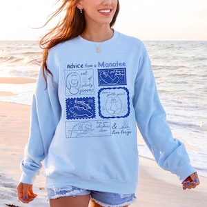 May include: Light blue sweatshirt with the text "Advice from a Manatee" and illustrations of manatees with phrases like "eat plenty greens" and "have a gentle spirit". The sweatshirt is a crew neck style.