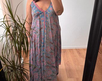 Könnte beinhalten: Ein langes, fließendes Kleid mit V-Ausschnitt und Spaghettiträgern. Das Kleid hat ein Paisley-Muster in Blau-, Rosa- und Grautönen. Der Stoff wirkt leicht und für warmes Wetter geeignet. Das Kleid hat eine lockere Passform.