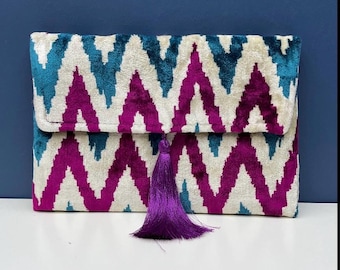 May include: A white clutch with a pink and teal chevron pattern and a purple tassel.