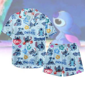 May include: Light blue pyjama set with a repeating pattern of Stitch, flowers, and the words "Ohana" and "Stitch." The set includes a short-sleeved button-up shirt and matching shorts. The shirt has white trim and the shorts have an elasticated waistband.