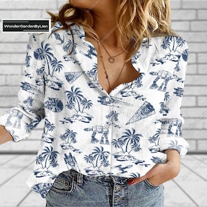 Könnte beinhalten: Weißes, langärmliges Hemd mit Knöpfen und einem blauen und weißen Druck von Palmen, Raumschiffen und AT-AT-Walkern. Das Hemd hat eine lockere Passform und einen V-Ausschnitt.