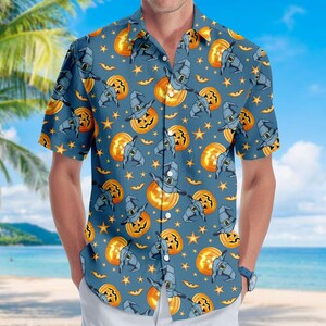 May include: A short-sleeved button-down shirt in a dusty blue color featuring an all-over pattern of orange jack-o'-lanterns, dark blue witch hats, and small yellow stars. The shirt has a classic collar and a front button placket.
