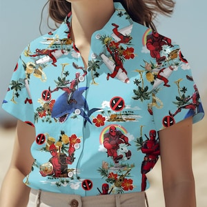 Könnte beinhalten: Ein blaues und weißes kurzärmeliges Hemd mit Knöpfen und einem tropischen Druck, der einen Superhelden zeigt, der auf einem Hai, einem Einhorn und einem Flugzeug reitet. Der Druck enthält auch Palmen, Regenbögen und andere tropische Elemente.