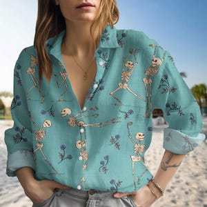 May include: A turquoise blue long-sleeved button-down shirt with a skeleton print. The shirt has a v-neck and a relaxed fit.